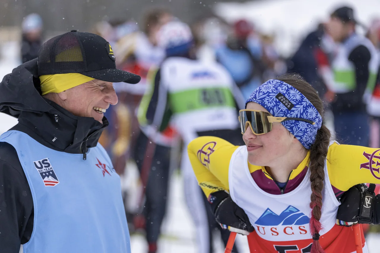 Marcin smiling and talking with a skier at a snowy race venue.